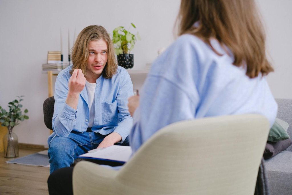A young man in therapy, gesturing towards therapist in a comfortable setting.